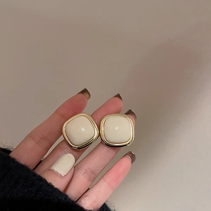 Gros plan détaillé d'une boucle d'oreille carrée perle crème avec cadre en métal doré vintage