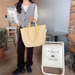 Close-up of yellow plaid tote bag with wide straps held by a model in a cafe setting