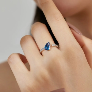 Close-up of blue teardrop-cut stone ring with micro-paved diamonds on silver band