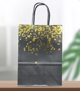 Detail of black kraft gift bag featuring shiny gold foil heart patterns and rope handles