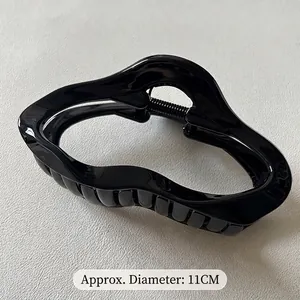 Detail view of 11cm black glossy hair claw clip with a wavy design on white leather