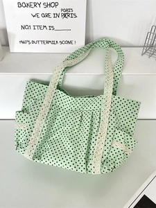 Green polka dot canvas tote bag with lace trim and side pockets on a white podium