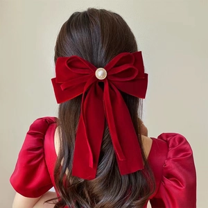 Macro shot of large red velvet bow hair clip with central pearl button on long wavy hair