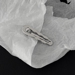 Detail of silver wavy metal hair clip with a polished mirror finish on textured background