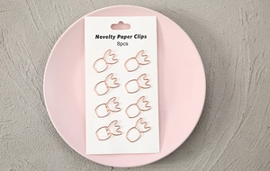 Set of 8 rose gold pineapple-shaped paper clips on white card in a ceramic dish