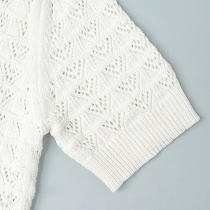 Detail of white pointelle knit top featuring intricate hollow patterns and ribbed cuffs