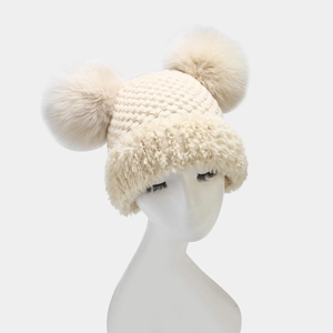 Close-up of knit winter beanie featuring two large faux fur pom-poms and plush lining