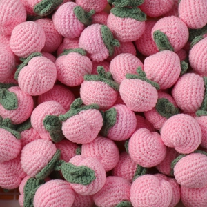 Detail of multiple handmade crocheted pink strawberry pendants with green leaves