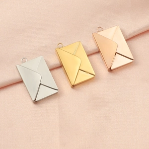 Close-up of envelope-shaped pendants in silver, gold and rose gold on pink silk fabric