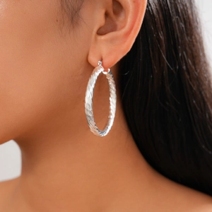 Macro shot of silver round hoop earring featuring detailed spiral texture on model