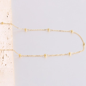 Detailed shot of a gold-plated stainless steel bead necklace on a textured stone surface
