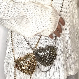 Detailed view of heart-shaped hollow metal bag with decorative chain on white sweater