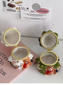 Detail of ceramic Christmas bear jewelry box with gold metal hinge on a pink book
