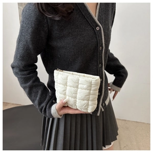 Close-up of a quilted white padded clutch bag held by a model in casual outfit