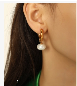Close-up of elegant gold hoop earrings with white pearl pendants worn by a model