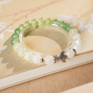 Macro detail of bead bracelet featuring gradient jade beads and a silver fish charm