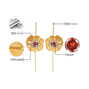 Detailed macro view of S925 silver gold-plated flower earrings with red garnet center
