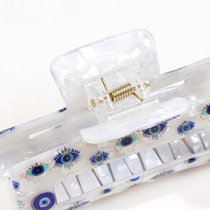 Macro detail of cream hair claw clip with evil eye pattern and golden metal spring