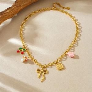 Golden necklace with cherry, mushroom, and bow charms on a minimalist textured background