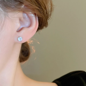 Close-up of a silver stud earring with a sparkling cubic zirconia stone on an ear