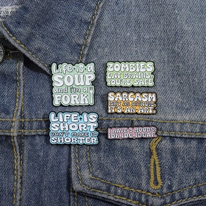 Five creative metal enamel pins with humorous quotes displayed on a blue denim jacket lapel