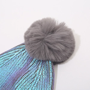 Metallic knit beanie with large grey faux fur pompom and iridescent blue-purple finish
