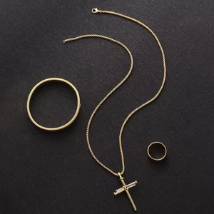 Detailed set of gold-plated nail cross pendant, matching bracelet and ring on dark surface