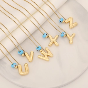 Gold letter necklaces U-Z with blue evil eye pendants on white marble tray