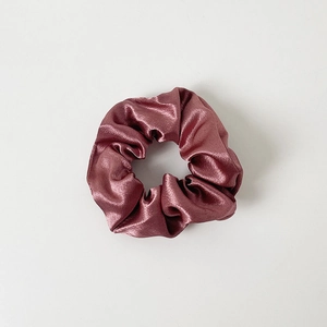 Close-up of a dusty rose satin scrunchie with glossy silk-like pleated fabric texture