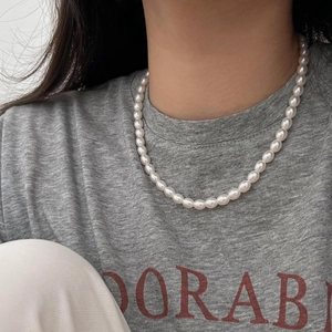 Detail view of a 925 sterling silver pearl necklace worn by a model on a grey shirt
