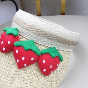Detail of children's straw sun visor featuring cute red strawberry fabric ornaments
