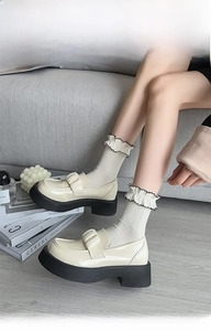 Close-up of cream patent leather platform loafers with bow detail and frilly socks