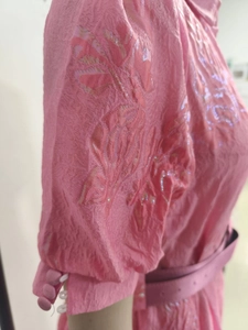 Close-up of pink jacquard fabric with floral patterns and sleeve button detail on a dress