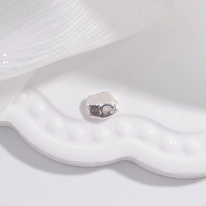 Macro detail of S925 sterling silver irregular faceted spacer bead on white ceramic tray