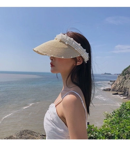 Detailed view of beige woven straw sun hat decorated with elegant white pearls on the edge