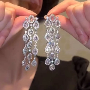 Boucles d'oreilles pendantes argentées avec cristaux gouttes sur fond de tenue noire