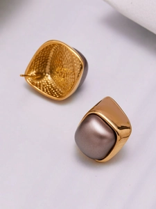 Close-up of geometric gold stud earrings featuring large grey pearls on textured fabric