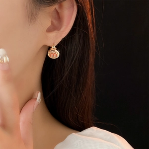 Close-up of a gold hoop earring with red enamel M letter charm worn by a model
