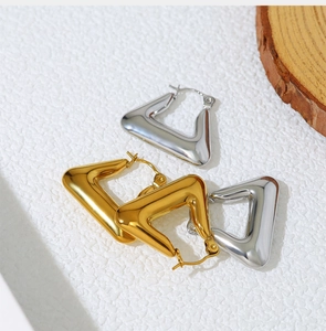 Detail of geometric triangle earrings in gold and silver finish on a stone surface