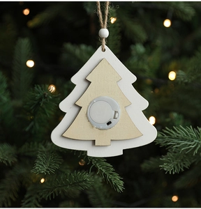 Detail of wooden Christmas tree ornament with light-up battery box and warm glow on a tree