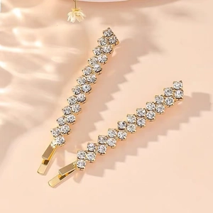 Close-up of gold-plated hair clips with sparkling clear rhinestones on a warm beige background