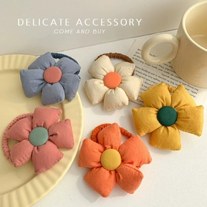 Close-up of five colorful fabric flower hair ties on a ceramic plate with detailed stitching