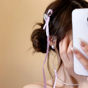 Detailed view of rhinestone hair clip with long purple flowing ribbons on model