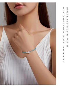 Sky blue braided leather bracelet with silver four-leaf clover charm worn on wrist