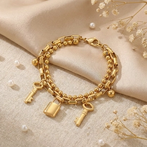 Detail view of double-layered gold chain bracelet with padlock and key charms