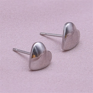 Close-up of polished silver heart earrings on a soft pink textured fabric background
