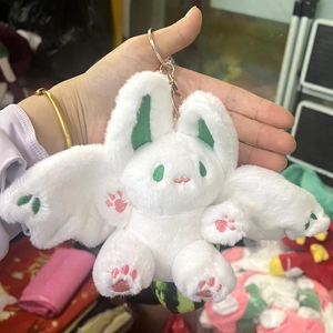 Detail of a white plush rabbit keychain with green bat wings held by hand in a warehouse