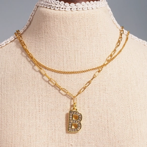 Detail of layered gold 'B' pendant necklace with zircon inlay on a model