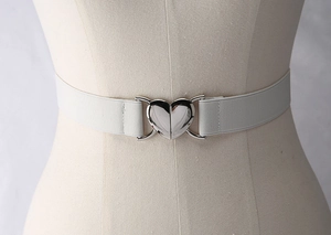 Détail d'une ceinture élastique blanche avec boucle métallique en forme de cœur argenté