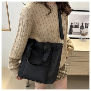 Detail of black nylon tote bag with front pocket shown in a lifestyle casual setting